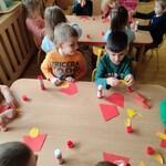 dzieci siedzące przy stoliku i wykonujące pracę plastyczną pt.