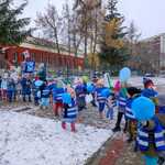 Dzieci idące w parach w niebieskich kamizelkach z balonami