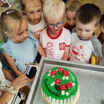 Kilkoro dzieci przygląda się tortowi grupy 