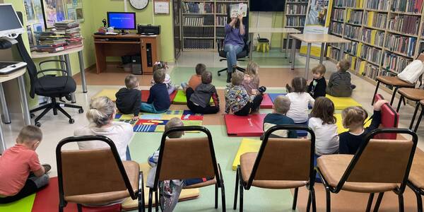 dzieci siedzące na dywanie w bibliotece słuchające czytanego opowiadania