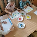 Dzieci przy stoliku stawiają kolorowe kropki na kartkach